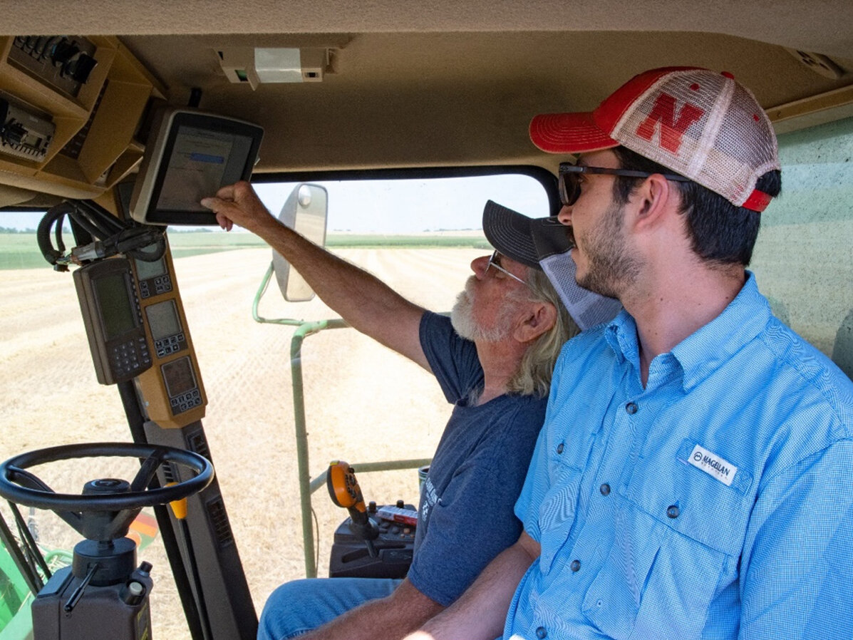 Two men inside tractor cab looking at software interface